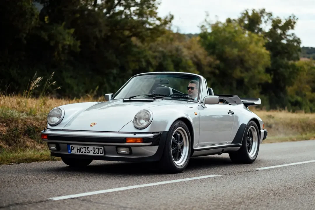 Voiture décapotable gris roulant sur route, modèle Porsche 930 convertible, arborant un aileron arrière