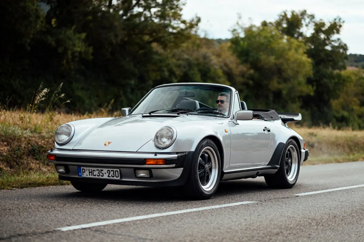 Voiture décapotable gris roulant sur route, modèle Porsche 930 convertible, arborant un aileron arrière