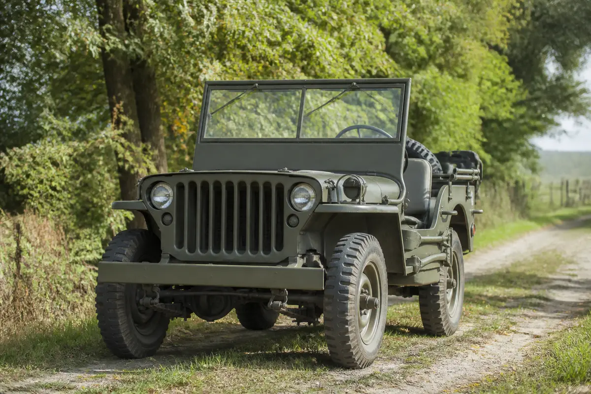 Ancienne jeep militaire sur chemin forestier, entourée de verdure et arbres majestueux