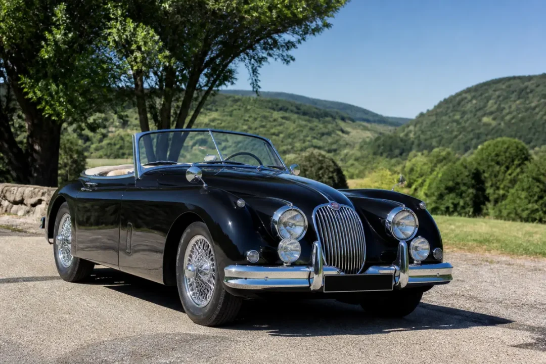 Voiture classique noire décapotable en plein air, modèle XK 150 Roadster devant paysage verdoyant