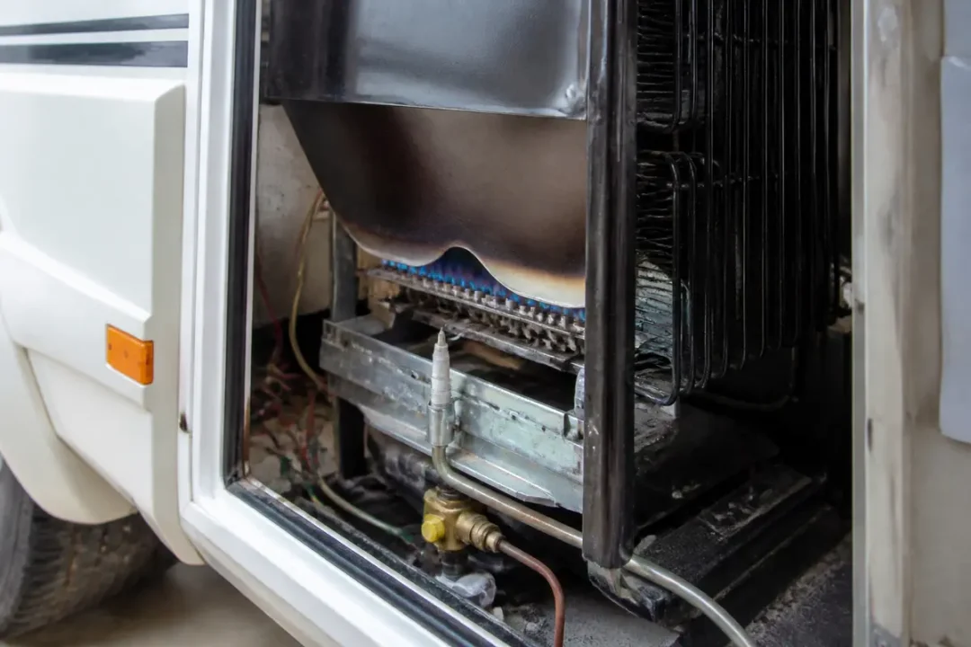 Intérieur d'un frigo à gaz pour camping-car avec brûleur allumé et tuyauterie visible