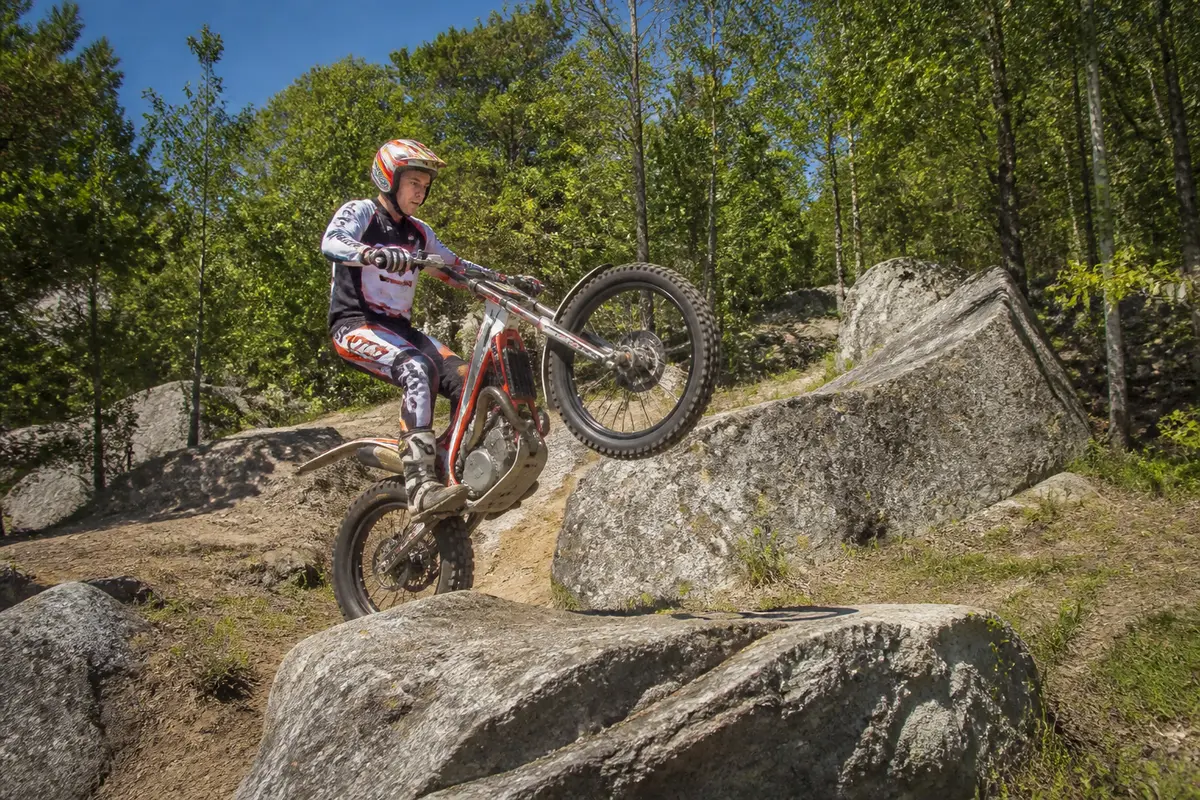 Un motard effectue un saut avec une moto de trial sur des rochers en forêt