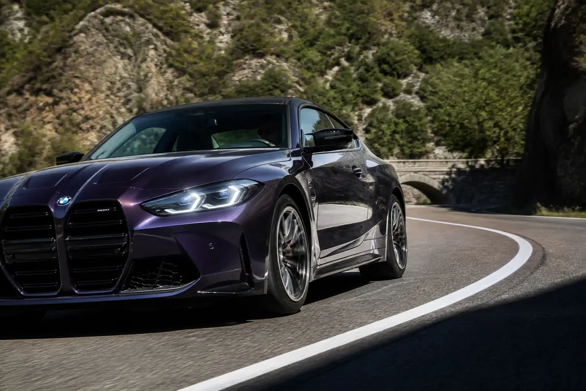 BMW M4 sportive roulant sur une route sinueuse en montagne, couleur violette élégante
